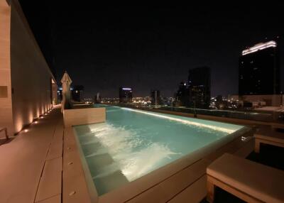 Night view of a lit rooftop pool with city skyline in the background