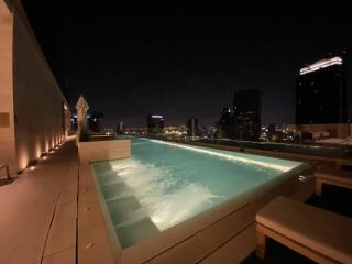 Night view of a lit rooftop pool with city skyline in the background