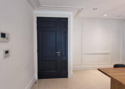 Interior view of a modern entryway with black door, control panels on the wall, and part of a wooden table with chairs