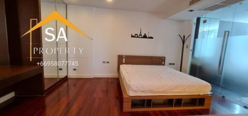 Spacious bedroom with wooden flooring, large bed, and glass partition