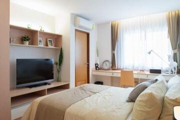 Well-lit bedroom with a bed, TV, desk, and window