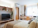 Well-lit bedroom with a bed, TV, desk, and window