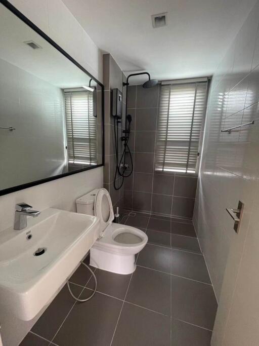 Modern grey-tiled bathroom with sink, toilet, and shower.