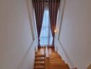 A well-lit staircase with wooden steps, leading to a floor with tall ceiling-height curtains.