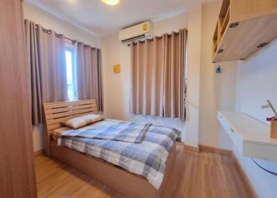 Bed with wooden headboard, window with curtains, air conditioner, wooden floor, wall-mounted desk with shelf