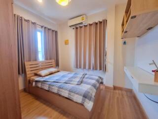 Bed with wooden headboard, window with curtains, air conditioner, wooden floor, wall-mounted desk with shelf