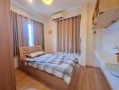 Bed with wooden headboard, window with curtains, air conditioner, wooden floor, wall-mounted desk with shelf