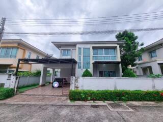 Exterior view of a two-story house with a carport and front garden