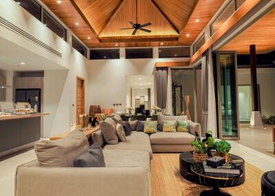 Modern, spacious living room with high wooden ceiling, large L-shaped sofa, glass doors, and contemporary decor