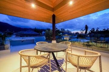 Outdoor balcony area with a round table and four wicker chairs under a wooden ceiling during sunset