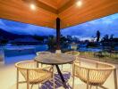 Outdoor balcony area with a round table and four wicker chairs under a wooden ceiling during sunset