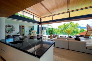 Modern open plan living room and kitchen with large windows, stylish furniture, and scenic view.