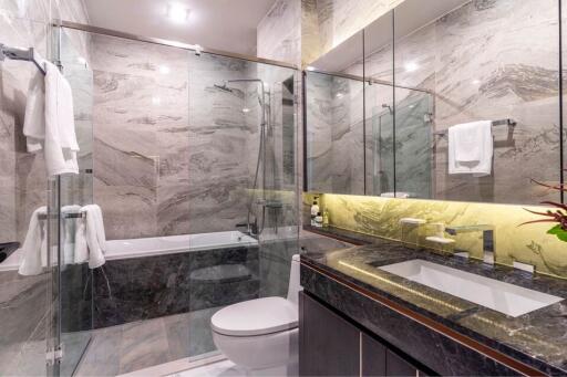 Modern bathroom with glass shower and bathtub, marble tiles, and illuminated mirror