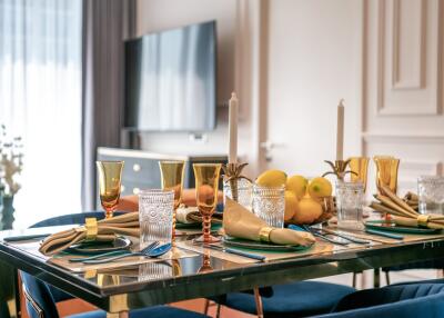 Elegant dining room setup with glass table, golden tableware, and a fruit bowl