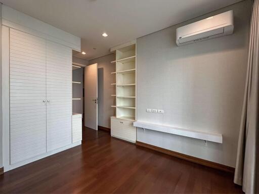 Modern bedroom with wooden flooring, built-in shelves, air conditioning, and wardrobe