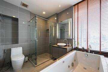 Modern bathroom with glass shower, bathtub, toilet, and large window with blinds