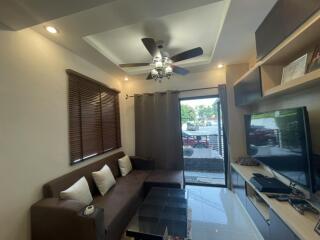 Modern living room with brown sofa, ceiling fan, large window with blinds, and TV setup