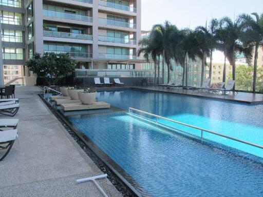 Outdoor pool area with lounge chairs, plants, and nearby building