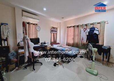 Bedroom with a messy layout including a bed, desk, chair, clothes, and a fan