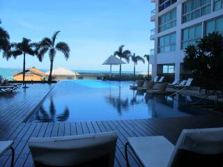 Outdoor pool area with lounge chairs and palm trees by a building