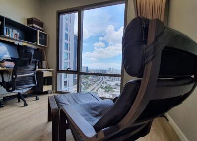 A well-lit home office with a desk, computer, and a large chair overlooking a city view