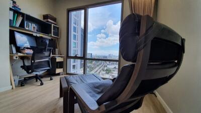 A well-lit home office with a desk, computer, and a large chair overlooking a city view