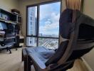 A well-lit home office with a desk, computer, and a large chair overlooking a city view