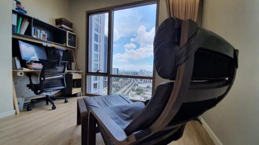 A well-lit home office with a desk, computer, and a large chair overlooking a city view