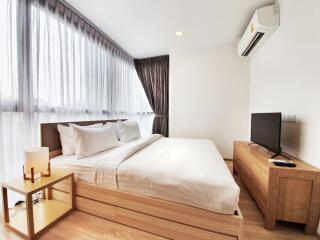 Modern bedroom with a large window, double bed, side table, and TV on a wooden stand