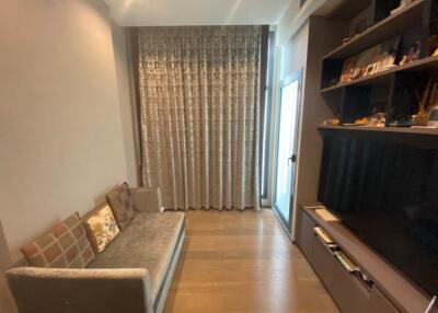 A cozy living room with a couch and a television, featuring floor-to-ceiling curtains and built-in shelving.