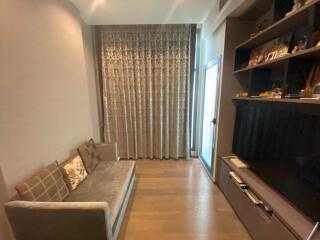 A cozy living room with a couch and a television, featuring floor-to-ceiling curtains and built-in shelving.