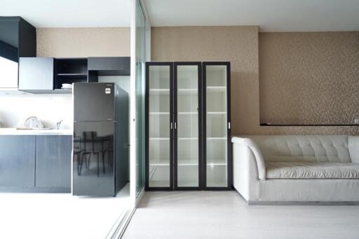 Modern living room with an open kitchen, glass-fronted cabinets, and a sofa.