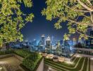 Night view of city skyline from rooftop terrace with greenery and seating area