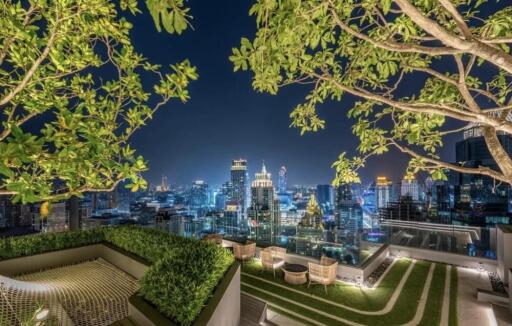 Night view of city skyline from rooftop terrace with greenery and seating area