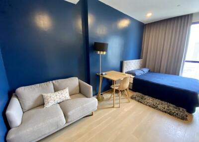 Modern bedroom with blue walls, bed, sofa, and desk