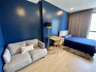 Modern bedroom with blue walls, bed, sofa, and desk