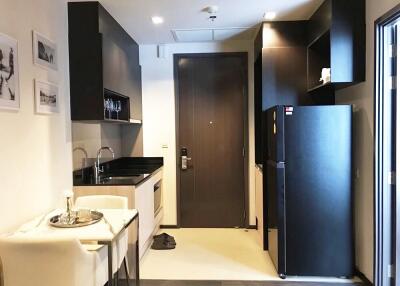 Modern compact kitchen with white cabinets and black countertops, a dining area with two chairs, and a fridge