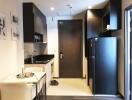 Modern compact kitchen with white cabinets and black countertops, a dining area with two chairs, and a fridge