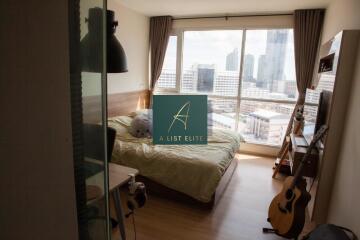 Bedroom with a large window overlooking city, wooden floor and furniture, and musical instruments