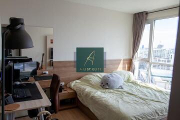 Bright bedroom with a desk, bed, large window with city view, and decor items