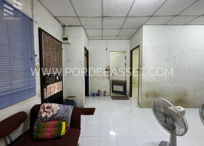 Simple living room with couch, blue window blinds, a standing fan, and a dirty white ceiling