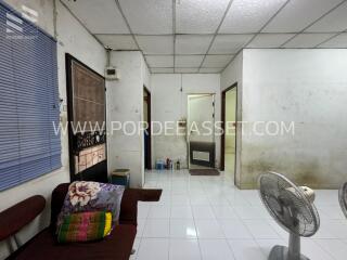 Simple living room with couch, blue window blinds, a standing fan, and a dirty white ceiling