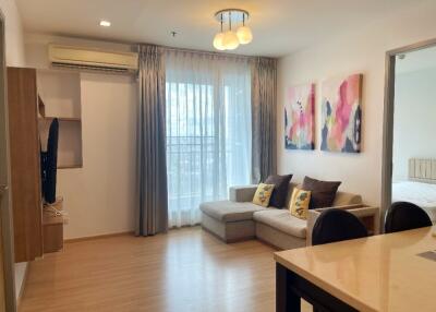 Modern living room with a sofa, wall-mounted TV, and large window.