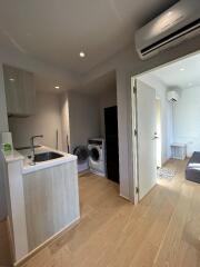 Modern apartment interior featuring a small kitchen area, laundry appliances, and a living space with wooden flooring and air conditioning.