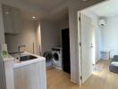 Modern apartment interior featuring a small kitchen area, laundry appliances, and a living space with wooden flooring and air conditioning.