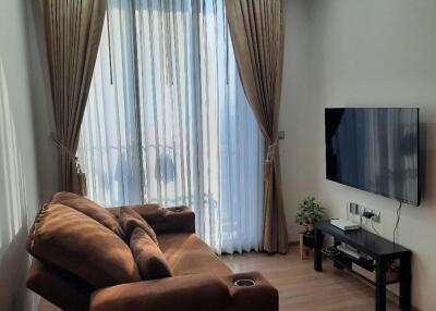 A cozy living room with a sofa, TV, and large window with curtains