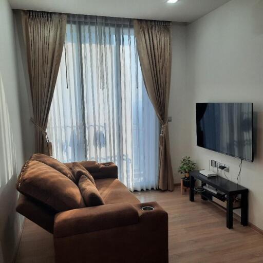 A cozy living room with a sofa, TV, and large window with curtains