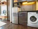 Modern kitchen area with appliances including a refrigerator, washing machine, and microwave