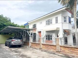 Exterior view of a two-story house with a carport and gated entrance