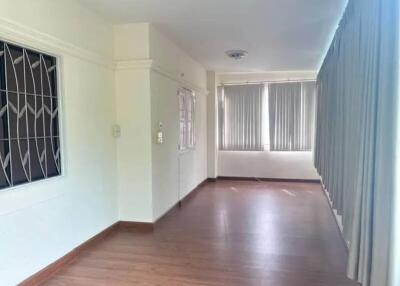 Empty living room with wooden flooring, windows with vertical blinds, and white walls